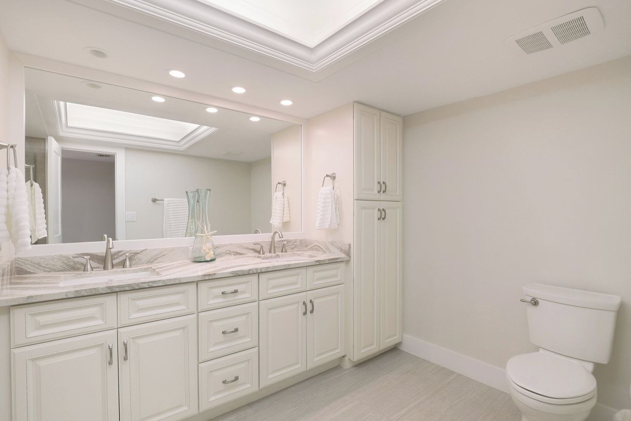A modern bathroom with a large mirror, white cabinetry, and a toilet.