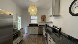 Een moderne keuken met witte kastjes, een zwart aanrecht, een roestvrijstalen afzuigkap en een wandklok.