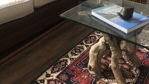 Een woonkamer met een bruine bank, een rieten bijzettafeltje met een lamp, een glazen salontafel en een kamerbreed tapijt met een patroon.