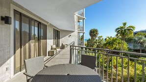 Ein Balkon mit Tisch und Stühlen, eine Treppe und Blick auf Palmen und das Meer.