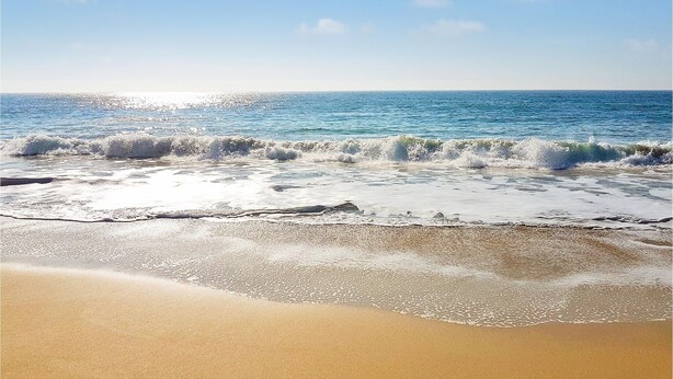 Une plage où les vagues se brisent sur le rivage, sous un ciel dégagé.