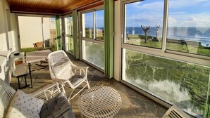 Une pièce baignée de lumière, avec un sol en pierre, des meubles en osier blancs et de grandes fenêtres donnant sur la mer.