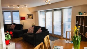 Ein modernes Wohnzimmer mit zwei schwarzen Sofas, einem Holzessttisch und einem Bücherregal.
