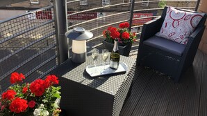 Ein Balkon mit Sitzgelegenheit im Freien, einem Tisch mit einer Weinflasche und Gläsern sowie einer Blumenkomposition.