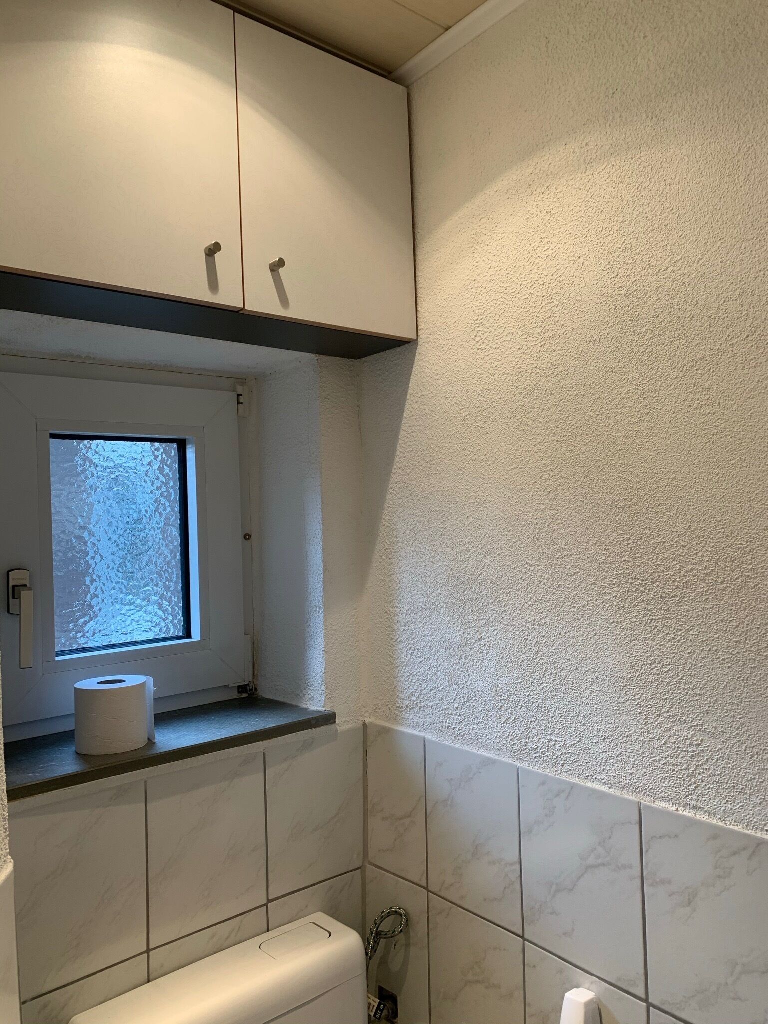 Ein Badezimmer mit Toilette, Fenster und Handtuchspender.