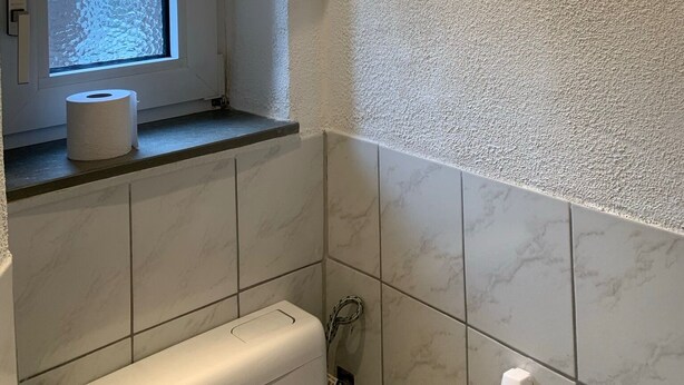 Un baño con inodoro, ventana y dispensador de toallas.
