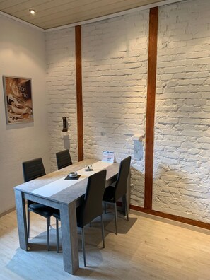 A conference room with a white brick wall, a wooden beam, and a table with chairs. - Our apartment is located on a residential street next to Prosperpark. (Bottrop)