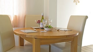 Une table de salle à manger ronde en bois, accompagnée de quatre chaises, une bouteille de vin, un bol de raisins et un verre.