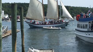 En segelbåt med flera segel, förtöjd vid en brygga, med en kyrka och andra båtar i bakgrunden.