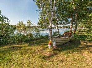 En båd ligger ved kaj nær en græsmark med træer og en sø i baggrunden.