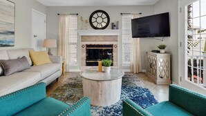Un salon comprenant un canapé, des fauteuils turquoise, une table basse, une cheminée, un téléviseur et un ventilateur de plafond.