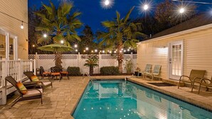 Un jardin avec une piscine, des meubles d’extérieur et des guirlandes lumineuses.