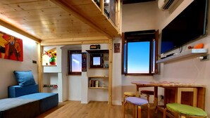 Una habitació acollidora amb sostre de fusta, un sofà blau, una taula petita amb caires i un televisor fixat a la paret.