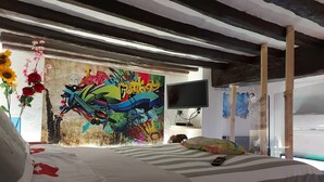 Un dormitori amb un llit, una televisió i un mural de colors a la paret.