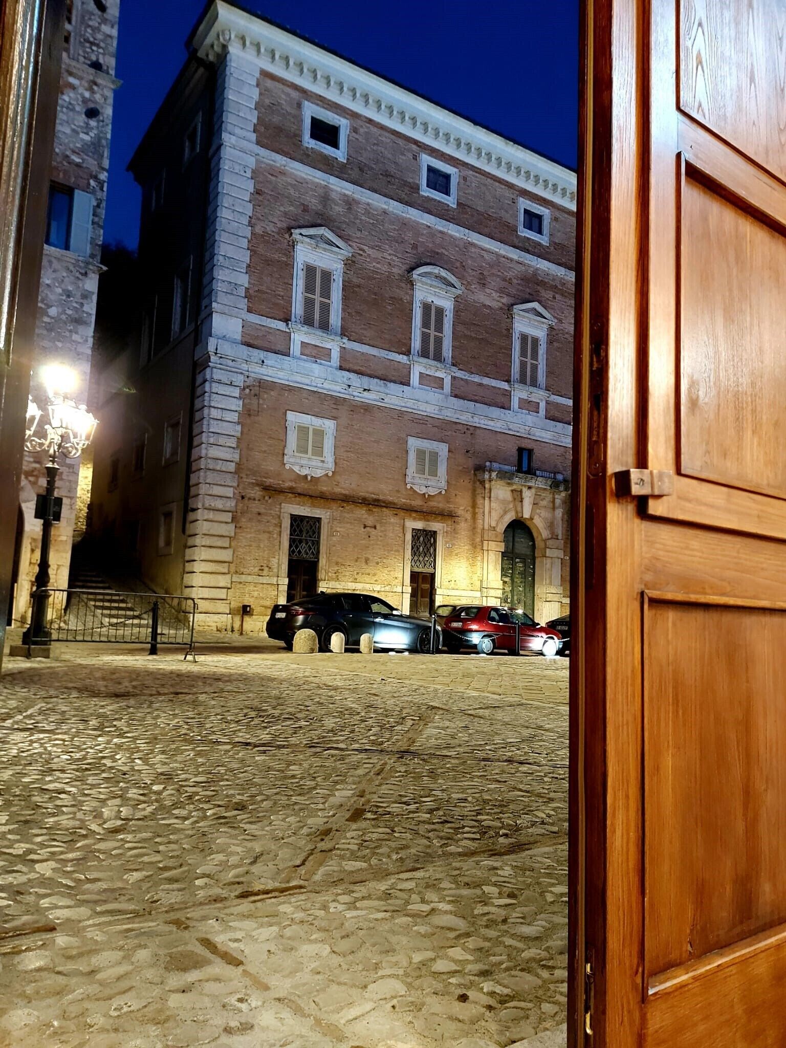 L’entrée d’un immeuble donnant sur une cour pavée, avec une porte en bois et un lampadaire.