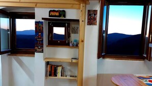 Interior acollidor d'una cabana amb un llit doble, prestatges de fusta, zona de menjador i grans finestres que ofereixen vistes panoràmiques.
