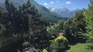 Eine gebirgige Landschaft mit einem Haus, umgeben von Bäumen und Grün.