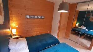 Ein Zimmer mit Holzwänden, einem Bett mit blauer Matratze, einem Nachttisch mit Lampe und einem Spiegel, der ein weiteres Bett reflektiert.