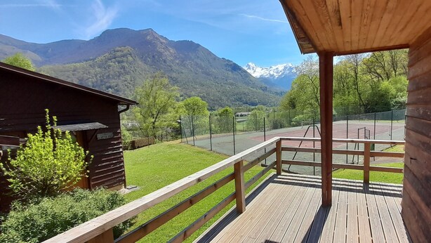 Eine Holzterrasse mit Blick auf einen Tennisplatz und Berge.