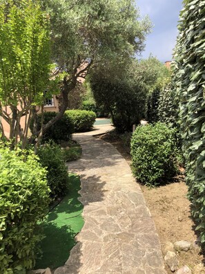 Un chemin de pierres dans un jardin, bordé de divers arbustes et arbres verts.
