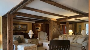 Un salon rustique avec des poutres apparentes, des canapés à motifs floraux et un fauteuil en bois.