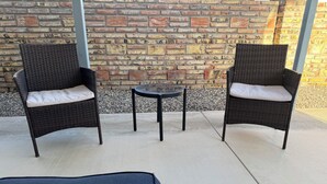 Two wicker chairs with white cushions and a small round table in front of a brick wall.