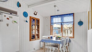 Un coin repas avec une nappe à carreaux, des chaises blanches, un buffet en bois et une fenêtre ornée de rideaux bleus.