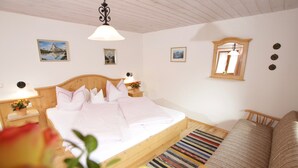 Quarto com cama de madeira, mesa de cabeceira com abajur, espelho e vista para a montanha pela janela.