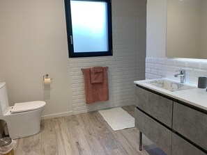 Ein modernes Badezimmer mit Toilette, Waschbecken mit Spiegel und einem Fenster über dem Waschbecken.
