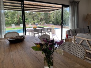 Ein Essbereich mit Holztisch, Stühlen und einem Blumenstrauß. Draußen befindet sich ein Pool und ein Garten mit Stühlen und einem Tisch.
