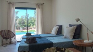 Ein Schlafzimmer mit zwei Betten, einem Sessel, einer Lampe und Blick auf einen Pool.