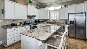 A kitchen with white cabinets, a large island with seating, stainless steel appliances, and a window providing natural light. - Nicely decorated home with private saltwater pool! Pet friendly! (Pensacola Beach)