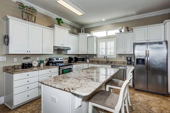 A kitchen with white cabinets, a large island with seating, stainless steel appliances, and a window providing natural light.