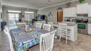 A spacious kitchen with white cabinets, a dining area with a patterned tablecloth, and a view of the outside. - Nicely decorated home with private saltwater pool! Pet friendly! (Pensacola Beach)