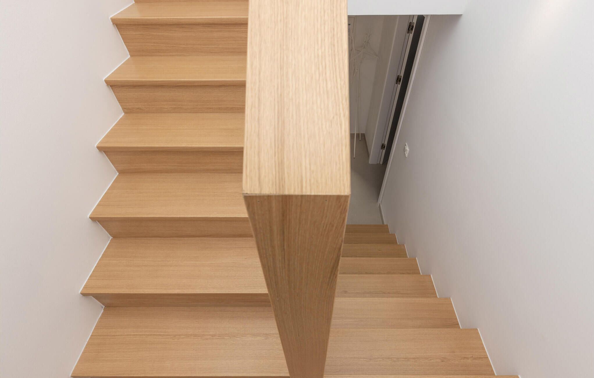 A wooden staircase with a modern design, leading to a room with white walls and a door.