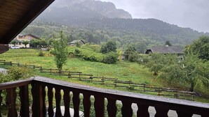 En utsikt från en balkong med utsikt över ett grönskande landskap, med hus och berg i fjärran.