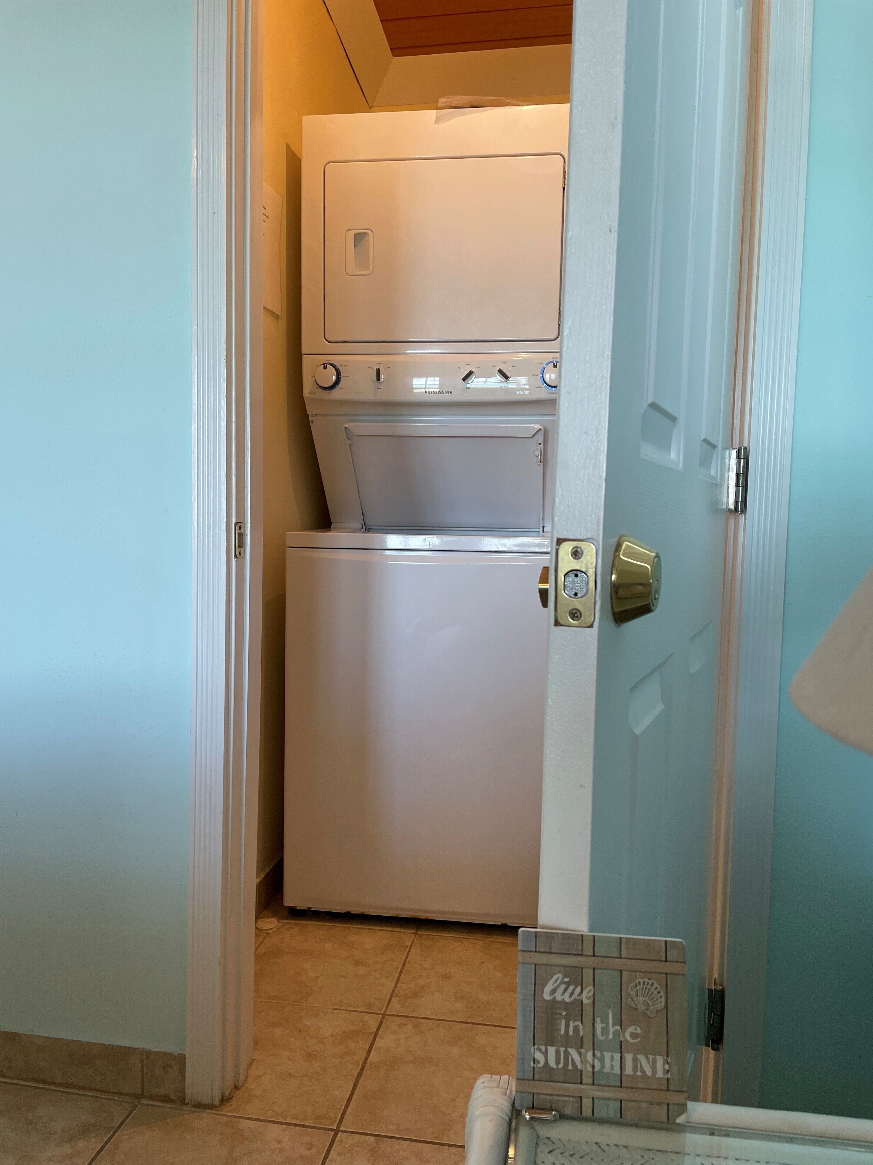 A compact laundry room with a washer and dryer, a door with a handle, and a small sign on the floor.