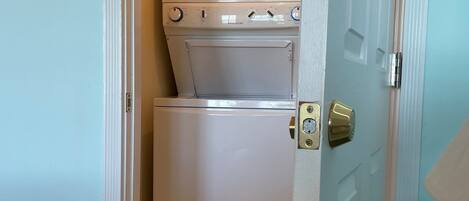 A compact laundry room with a washer and dryer, a door with a handle, and a small sign on the floor.