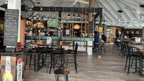 An indoor restaurant with high ceilings, exposed beams, and a bar area. Tables and chairs are arranged for dining. - Exuma Sol - Stunning Views from this Oceanfront Beach Cottage (George Town)
