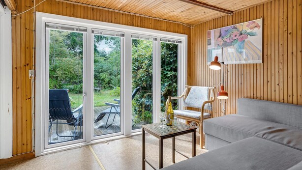 A room with a wooden ceiling, a grey sofa, a table with a bottle and glasses, and a bench. - 2 bedroom gorgeous home in Vig (Vig)