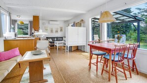 A spacious living area with a wooden dining table, red chairs, a white sofa, and a kitchen area with a white cabinet and a microwave. - 2 bedroom gorgeous home in Vig (Vig)