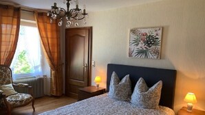 A bedroom with a bed, two bedside lamps, a chair, a radiator, a door, and a chandelier. - ALSACE COSY GITE 3 BEDROOMS 2 BATHROOMS (BUHL)