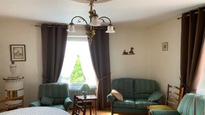 A cozy living room with a round table, two armchairs, a sofa, a chandelier, and a window with curtains. - ALSACE COSY GITE 3 BEDROOMS 2 BATHROOMS (BUHL)