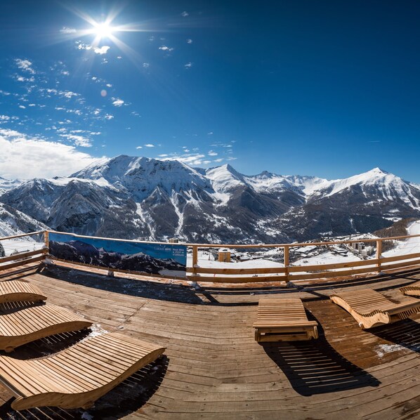 A wooden deck with lounge chairs overlooking a snowy mountain range.