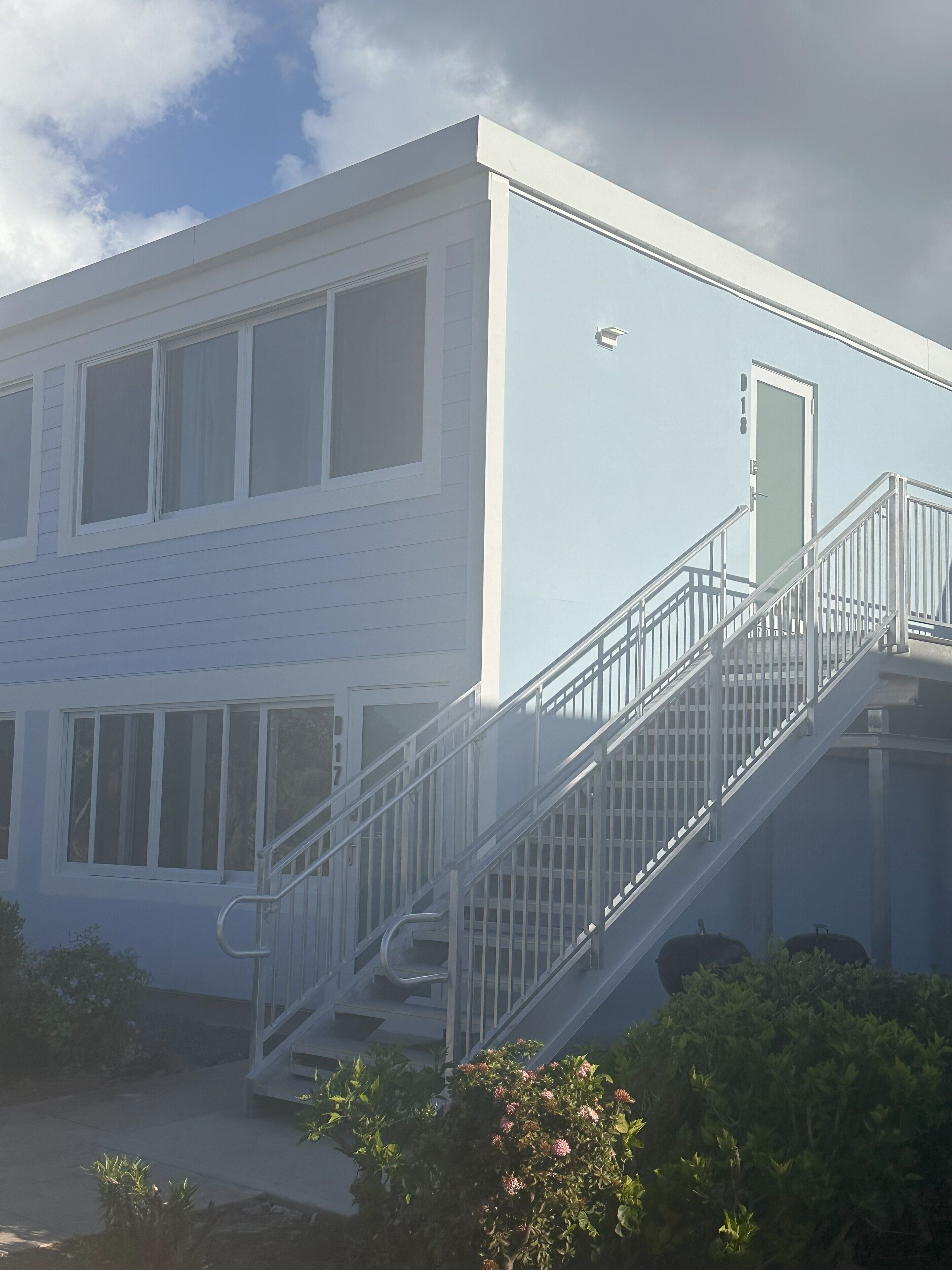 Un bâtiment moderne à l’extérieur blanc, doté de grandes fenêtres et d’un escalier métallique menant à l’entrée.