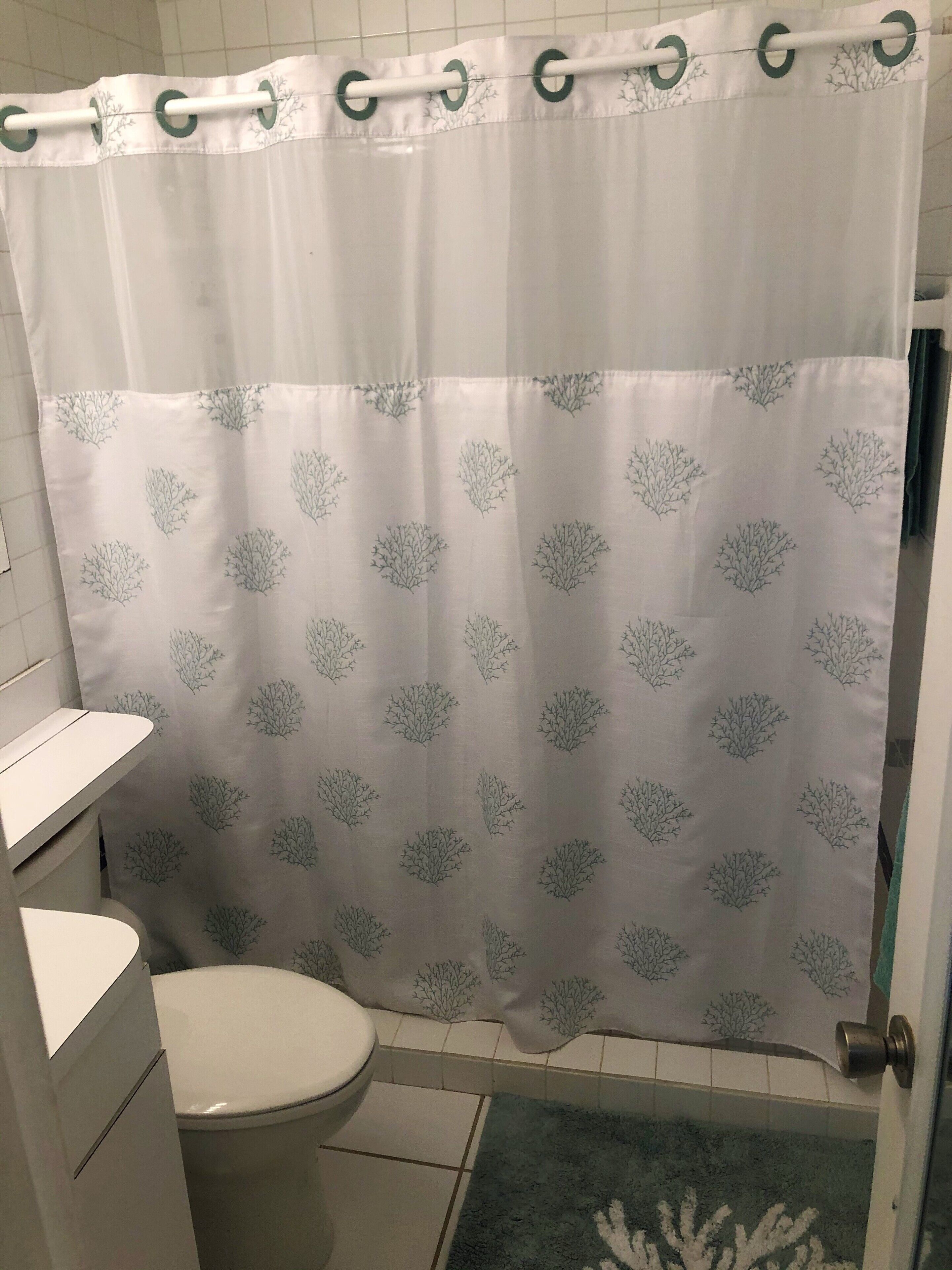 Een badkamer met een wit toilet, een witte wastafel en een douchegordijn met een boommotief.