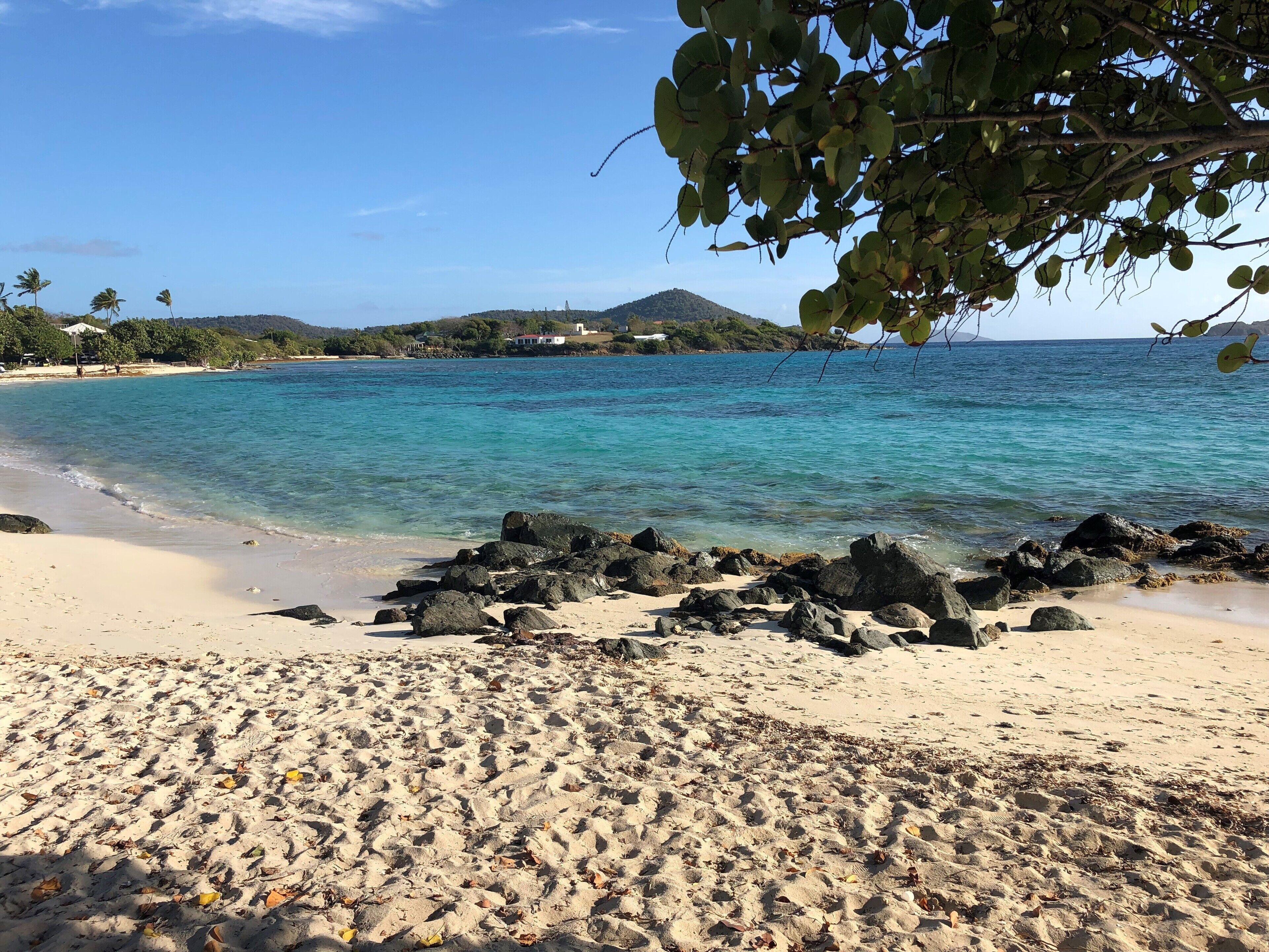 A beach with clear turquoise water, sandy shore, and rocky outcrops.
