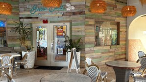 An indoor seating area with round tables and wicker chairs, a menu board, and a wall with a wooden plank design.