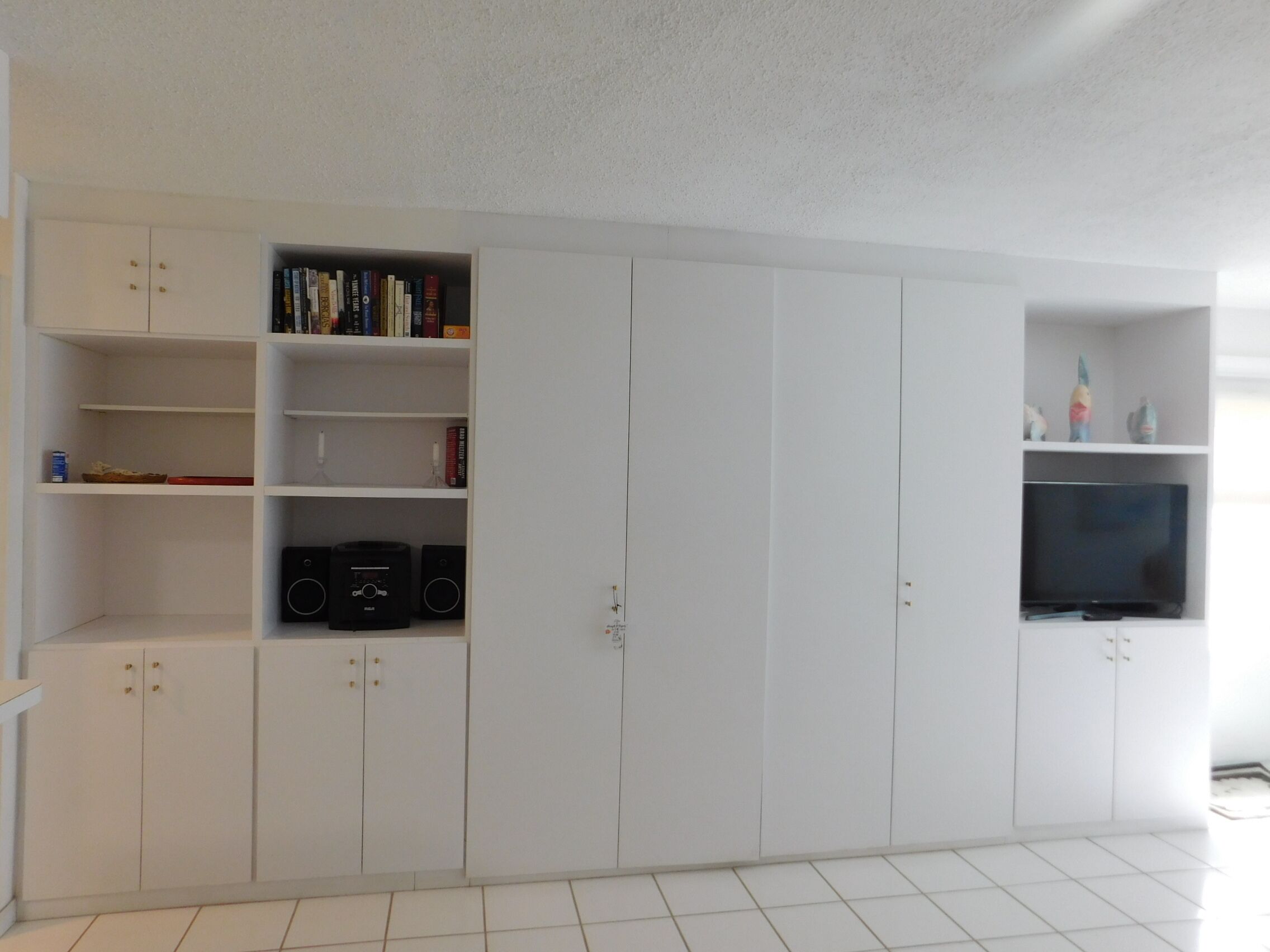 Una habitación amplia con armarios blancos, un televisor de pantalla plana y una estantería.