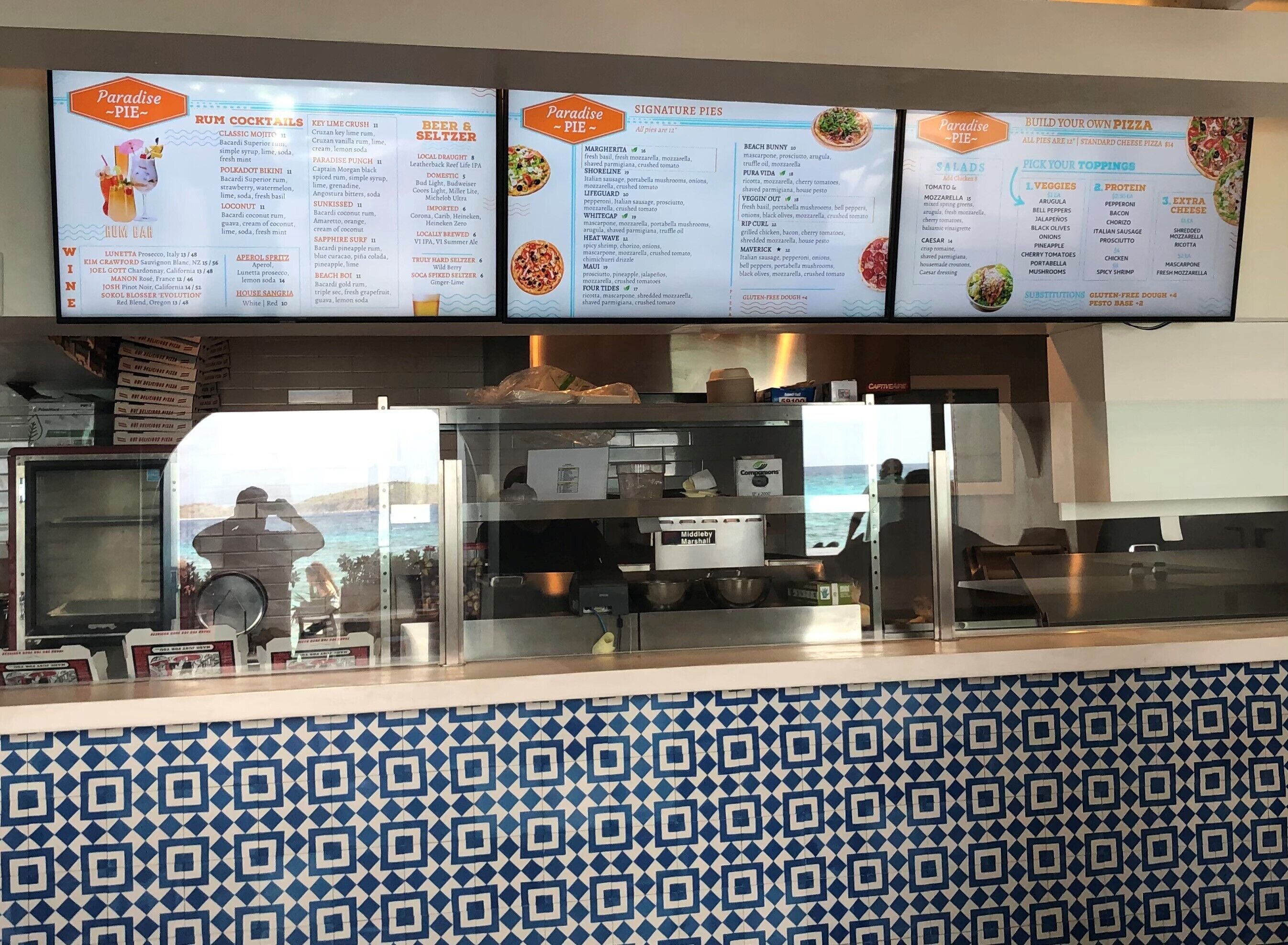 Un comptoir de restaurant avec un tableau affichant les différentes boissons et pizzas proposées.